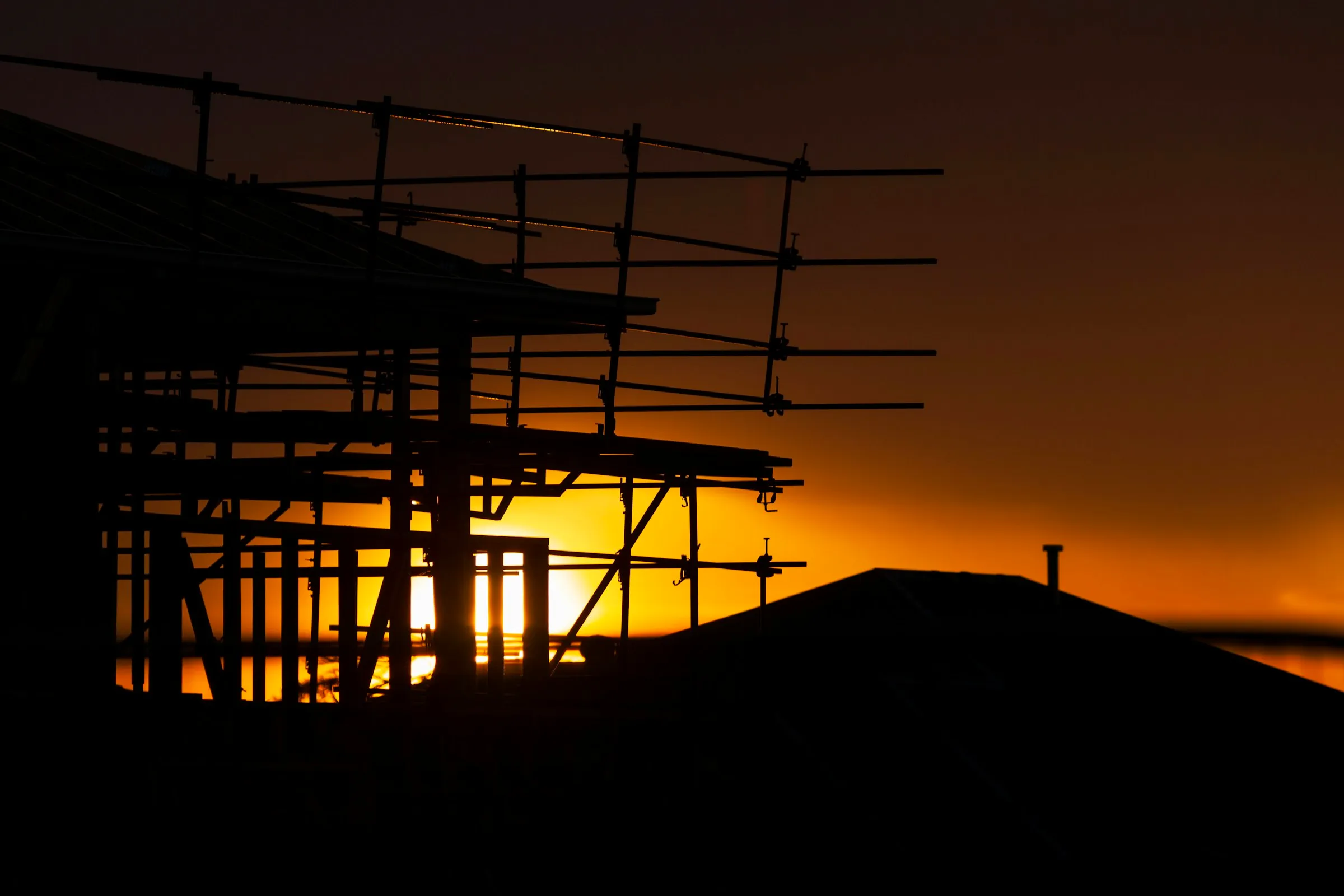 Construction scaffolding silhouetted against a low amber sun